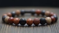 Natural stone beaded bracelet with brown, black and beige gemstones arranged in pattern on dark wooden surface, selective focus on spherical beads.
