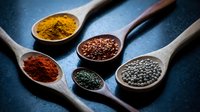 Colorful aromatic spices in wooden spoons on dark blue background. Turmeric, paprika, herbs and peppercorns for cooking and seasoning food preparation.