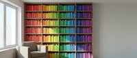 Colorful rainbow bookshelf with organized books by color spectrum in modern home library interior with reading chair and natural window light.