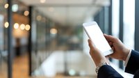Person holding smartphone with blank white screen in modern office lobby or corporate building hallway with blurred background and warm lighting for app mockup and business technology use.