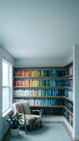 Cozy reading nook with rainbow organized bookshelf, comfortable armchair and natural light from window creating peaceful home library corner.