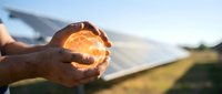 Young adult male hand holding glowing orb of light against solar panel and field background, representing renewable energy, sustainability, and clean power technology.
