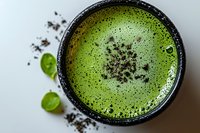 Frothy green matcha latte in ceramic bowl with cocoa nibs and fresh mint leaves on white marble surface for healthy beverage and wellness content.