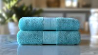Plush turquoise cotton bath towels neatly folded and stacked on reflective surface, showing luxurious texture and softness for spa and bathroom decor.