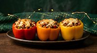 Colorful stuffed bell peppers filled with rice, meat and vegetables on dark plate with festive golden lights creating warm holiday atmosphere.