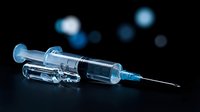 Medical syringe with needle and glass vial on dark background with blue bokeh lights for healthcare and vaccination concepts.
