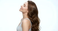Young Caucasian woman with long wavy brown hair in profile, eyes closed, peaceful expression, wearing gray tank top on white background for wellness concepts.