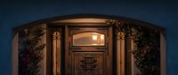 Elegant wooden front door with warm lighting and decorative glass panels framed by lush greenery creating welcoming home entrance at dusk.