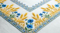Embroidered linen tablecloth corner with golden wheat stalks and blue flowers in traditional folk style pattern on white fabric background.