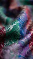 Colorful silk fabric with intricate woven patterns in green, blue, red and purple hues creating luxurious textile background for fashion and craft projects.