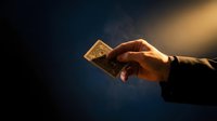 Hand holding glowing golden square object against dark background with warm light, suitable for spirituality, technology, wealth, and business concepts.