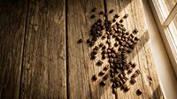 Roasted coffee beans scattered on rustic wooden planks with warm natural lighting creating cozy cafe atmosphere for beverage branding and culinary designs.