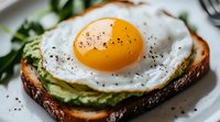Sunny side up egg on avocado toast with black pepper seasoning, fresh herbs and dark bread slice, served on white plate, macro food photography.