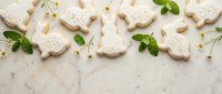 White decorated cookies shaped like doves arranged on marble surface with green leaves and scattered crumbs for bakery designs.