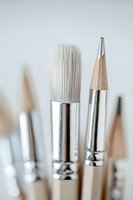 Close-up macro shot of white artist brush and wooden pencil with silver metal ferrules against light background, selective focus on bristles and tip.