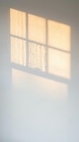 Warm sunlight streams through a six-pane window onto a neutral wall, creating geometric shadows and soft golden light patterns for interior design and architectural projects.