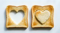 Two golden toasted bread slices with heart-shaped cutouts on white background, one empty and one filled with heart piece for romantic breakfast concept.