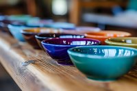 Colorful ceramic bowls arranged on wooden surface in pottery workshop studio for handmade crafts and artistic creation projects.
