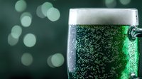 Cold glass of green beer with foam and bubbles on dark background with bokeh lights, festive St Patrick's Day celebration drink photography.