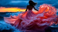 Young woman in flowing pink dress stands against dramatic sunset sky and ocean waves, fabric billowing dramatically in wind creating ethereal movement effect.