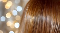 Silky smooth brown hair close-up with soft bokeh lights in background creating glamorous beauty salon atmosphere. Professional haircare and styling concept.