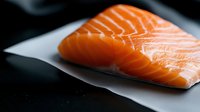 Fresh raw salmon fillet with visible texture and marbling on white paper against dark background, macro food photography for restaurant menu and culinary design.