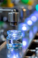 Electronic cigarette tank with blue illumination and metallic atomizer floating above glass container on blurred bokeh background, macro photography.