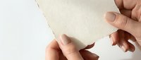 Young adult with light skin tone holding and tearing blank beige paper sheet, isolated on white background for design mockups, presentations, and creative projects.