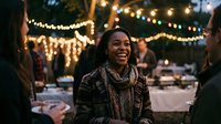 Young African American woman laughing joyfully at outdoor evening market with warm string lights creating festive atmosphere for social gatherings and celebrations.