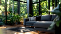 Modern sunroom interior with gray sectional sofa, potted plants and natural sunlight streaming through floor-to-ceiling windows creating peaceful atmosphere.