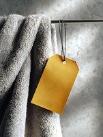 Yellow blank price tag hanging on soft gray towel against blurred background, selective focus on label creates modern minimalist composition for retail and spa.