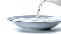Pouring fresh milk into white ceramic plate creating dynamic splash and ripple effect against light background, showcasing liquid motion and fluidity.
