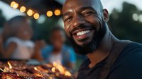 Happy African American man smiling at outdoor evening gathering with warm string lights and friends in background for social events and celebrations.
