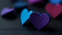 Colorful paper hearts in purple and blue tones on dark background with selective focus creating romantic mood. Suitable for Valentine's day designs and love themes.
