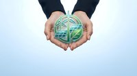 Business hands holding green earth globe with renewable energy symbols representing environmental sustainability and corporate responsibility.