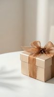 Elegant beige gift box with golden brown silk ribbon bow on white marble surface with soft natural lighting for special occasions and celebrations.