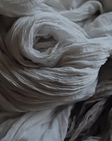 Delicate folds of white fabric create abstract swirling patterns in monochromatic composition, highlighting texture and movement through light and shadow play.