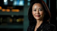 Professional Asian businesswoman in elegant black blazer standing confidently in modern office environment with city lights bokeh background at night.