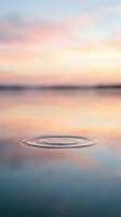 Serene lake at sunrise with concentric ripples spreading across calm water surface, soft pastel sky reflecting pink and gold tones for meditation and wellness content.