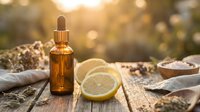 Amber glass dropper bottle with essential oil next to fresh lemon slice on rustic wooden surface with warm golden sunlight and natural spa ingredients.