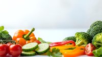 Fresh colorful vegetables including broccoli, tomatoes, peppers and cucumbers arranged on white surface for healthy cooking and nutrition concepts.