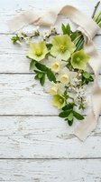 Spring bouquet of hellebores, daffodils, and cherry blossoms with linen ribbon on rustic white wooden background, flat lay.