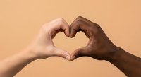 Two diverse hands forming heart shape symbol representing unity love friendship and racial harmony against warm beige background for social campaigns.