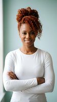 Confident African American woman with curly red hair in white long sleeve shirt crossing arms and smiling at camera in modern office setting.