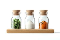 Three glass spice jars with cork lids on wooden holder containing dried herbs, white salt, and orange spice mix against white background, minimalist kitchen storage solution.
