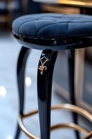 Elegant bar stool with quilted navy blue leather seat, black glossy frame decorated with gold ornamental detail, modern luxury furniture piece on blurred background.