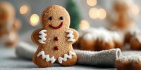 Gingerbread man cookie with white icing decoration standing on kitchen counter with warm bokeh lights and baked goods in background for holiday baking.