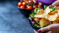 Fresh corn tortilla chips served with mixed green salad and cherry tomatoes in black ceramic bowls on dark background. Healthy Mexican food appetizer concept.
