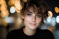 Young woman with short wavy brown hair, fair complexion, and freckles smiling at camera against blurred bokeh lights background for portrait and lifestyle use.