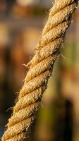 Close-up of weathered natural fiber rope with frayed edges and twisted texture against blurred background for nautical and rustic design projects.